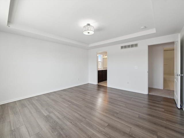 unfurnished room featuring dark wood-type flooring, a tray ceiling, visible vents, and baseboards