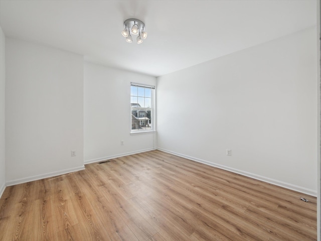 unfurnished room featuring light wood finished floors, visible vents, and baseboards