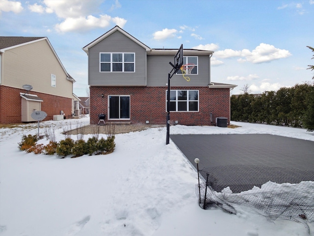 snow covered rear of property with central air condition unit and brick siding