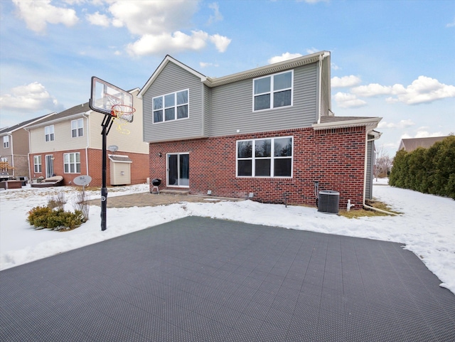 snow covered property featuring central air condition unit and brick siding