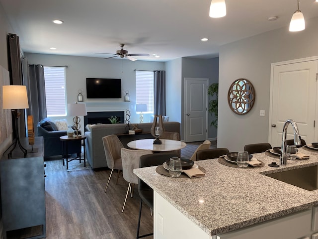 kitchen featuring a fireplace, a sink, open floor plan, hanging light fixtures, and light stone countertops