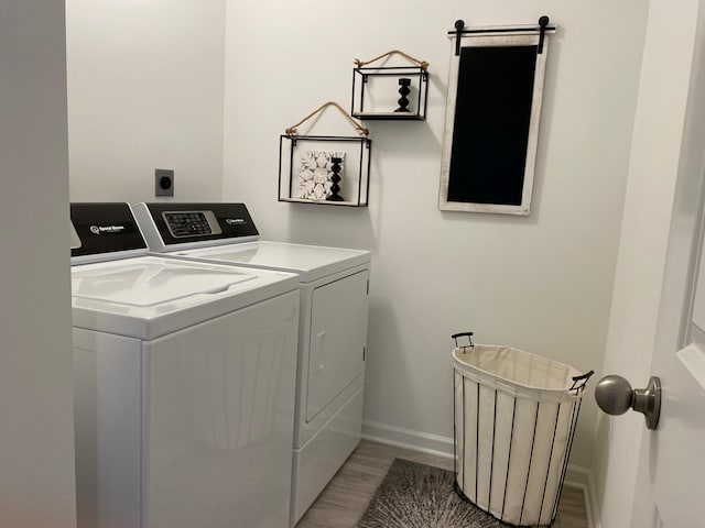 clothes washing area with laundry area, washing machine and dryer, baseboards, and light wood-style flooring