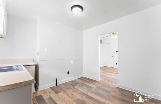 unfurnished dining area featuring light wood-type flooring, a sink, and baseboards