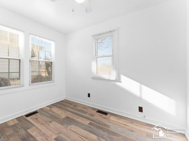 unfurnished room with a wealth of natural light, visible vents, and wood finished floors