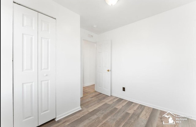 unfurnished bedroom with a closet, wood finished floors, visible vents, and baseboards