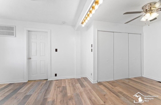 unfurnished bedroom featuring a textured ceiling, visible vents, baseboards, light wood-style floors, and a closet