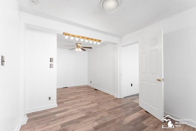 empty room with ceiling fan, a textured ceiling, baseboards, and wood finished floors