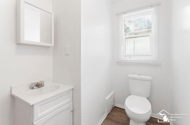 half bathroom with toilet, wood finished floors, vanity, and baseboards