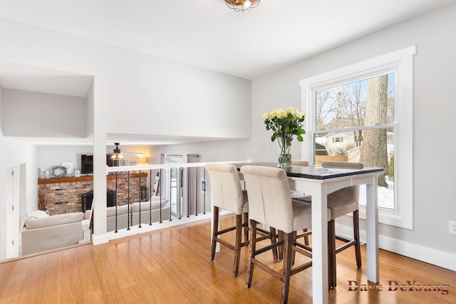 dining room with a brick fireplace, a ceiling fan, baseboards, and wood finished floors