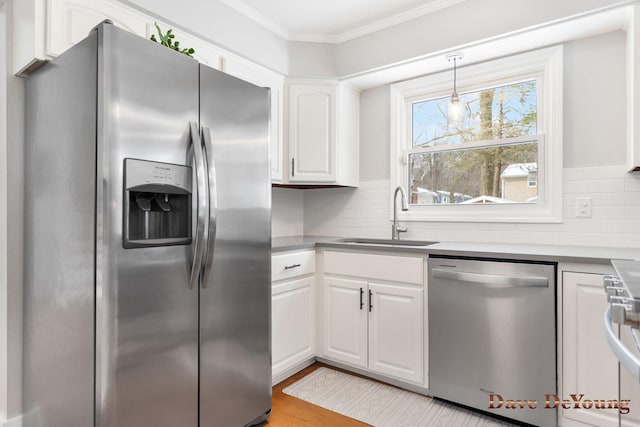 kitchen with stainless steel appliances, a sink, white cabinetry, decorative backsplash, and crown molding