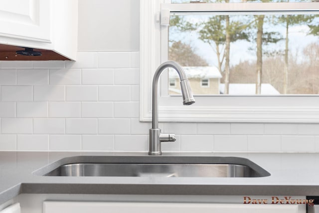 details featuring dark countertops, decorative backsplash, white cabinets, and a sink