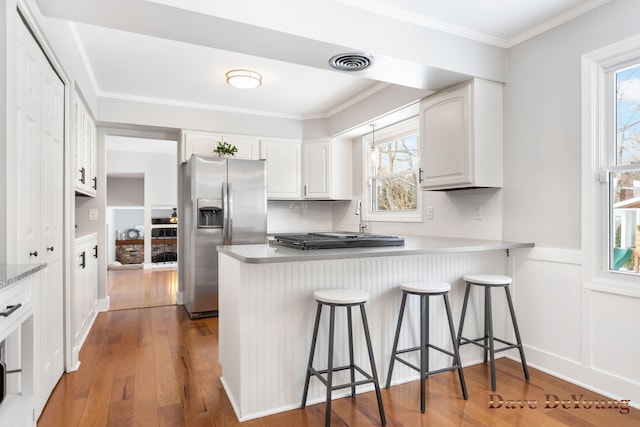 kitchen featuring a breakfast bar area, a peninsula, white cabinets, light countertops, and stainless steel fridge with ice dispenser