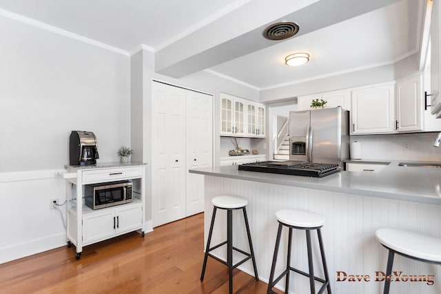 kitchen with stainless steel appliances, white cabinets, glass insert cabinets, and a kitchen bar