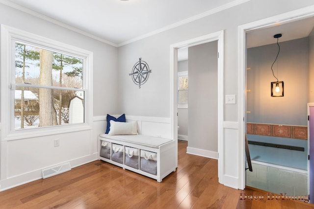 living area with a healthy amount of sunlight, crown molding, visible vents, and wood finished floors