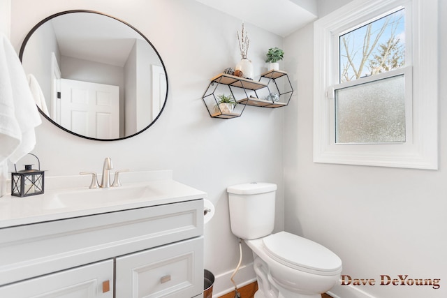 half bathroom with baseboards, vanity, and toilet