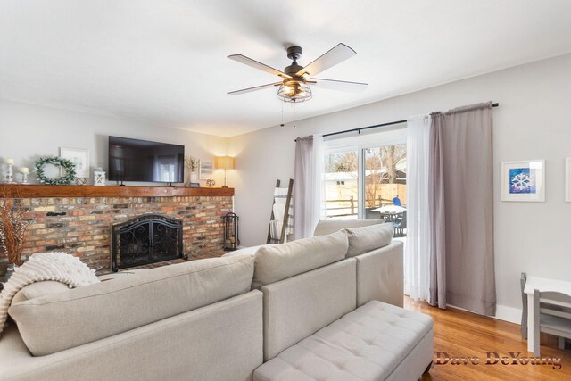 living area with a brick fireplace, baseboards, a ceiling fan, and light wood-style floors