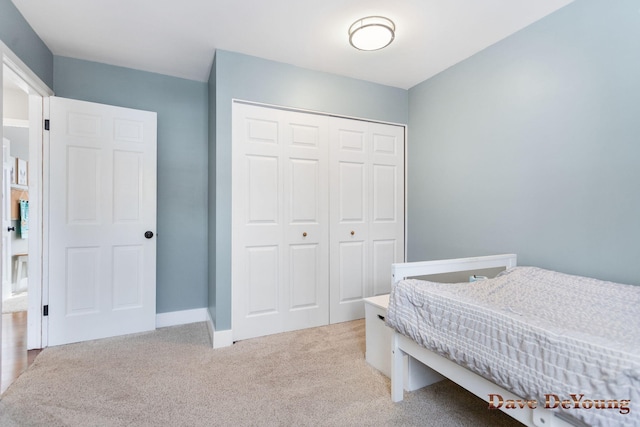 bedroom with baseboards, a closet, and light colored carpet