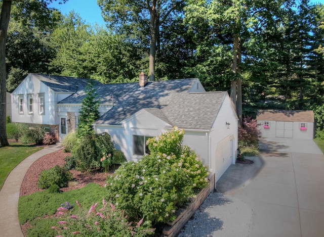 view of side of property featuring a storage shed, concrete driveway, a chimney, roof with shingles, and an attached garage