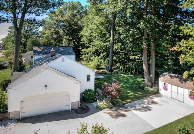 exterior space with a shingled roof, an outdoor structure, concrete driveway, and a yard