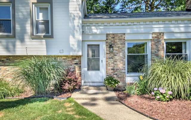 property entrance featuring brick siding and roof with shingles