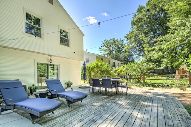 wooden deck featuring fence, a playground, and outdoor dining space