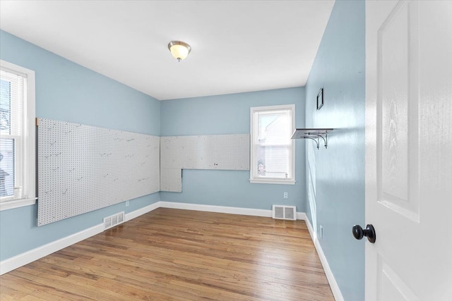 empty room with light wood-type flooring, visible vents, and baseboards