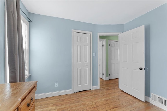 unfurnished bedroom with light wood-type flooring, a closet, visible vents, and baseboards