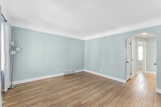 empty room with arched walkways, light wood finished floors, visible vents, and baseboards