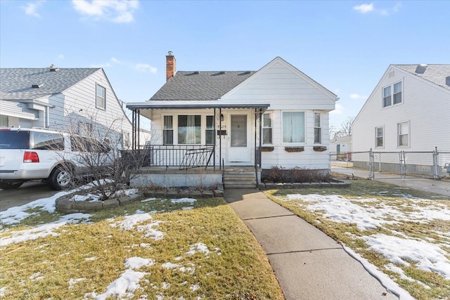 bungalow featuring a chimney, a shingled roof, covered porch, a lawn, and fence