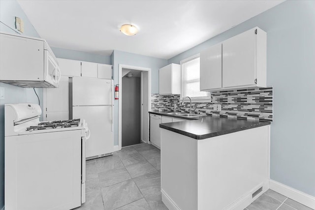 kitchen featuring dark countertops, decorative backsplash, white cabinetry, a sink, and white appliances