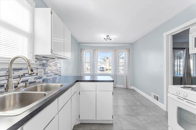 kitchen with decorative backsplash, dark countertops, white gas range, white cabinetry, and a sink