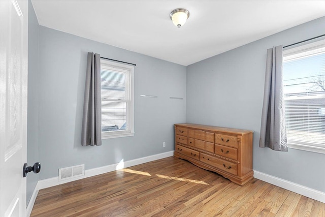 unfurnished bedroom featuring multiple windows, wood finished floors, visible vents, and baseboards