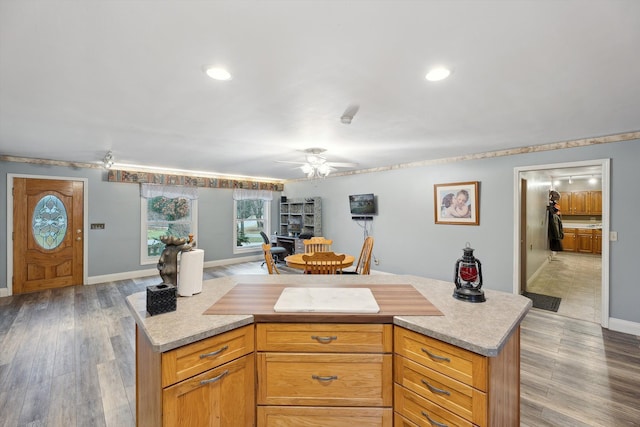 kitchen with light countertops, a ceiling fan, a kitchen island, wood finished floors, and baseboards