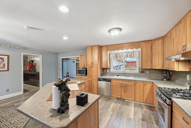 kitchen with decorative backsplash, light wood-style floors, appliances with stainless steel finishes, under cabinet range hood, and a sink