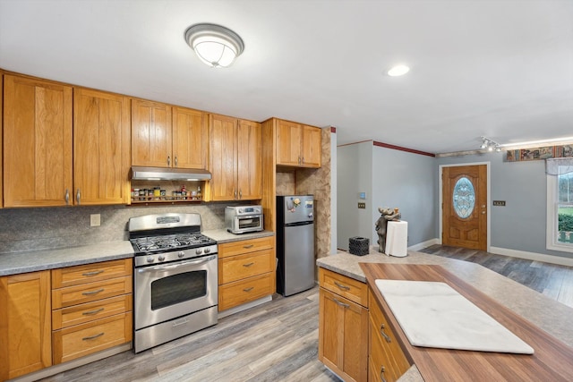 kitchen with tasteful backsplash, light wood-style flooring, stainless steel appliances, light countertops, and under cabinet range hood