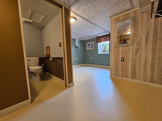 bathroom featuring finished concrete flooring, visible vents, toilet, wooden walls, and baseboards