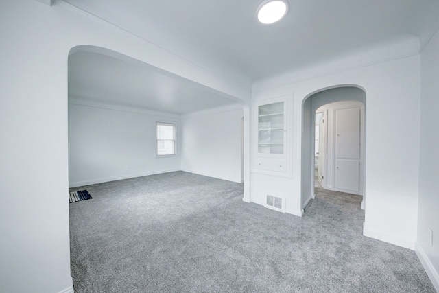 carpeted spare room featuring baseboards, visible vents, arched walkways, and built in features