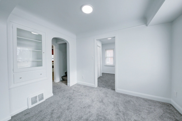 carpeted empty room with arched walkways, stairs, visible vents, and baseboards