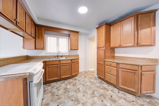 kitchen featuring brown cabinetry, a sink, baseboards, and white electric range oven