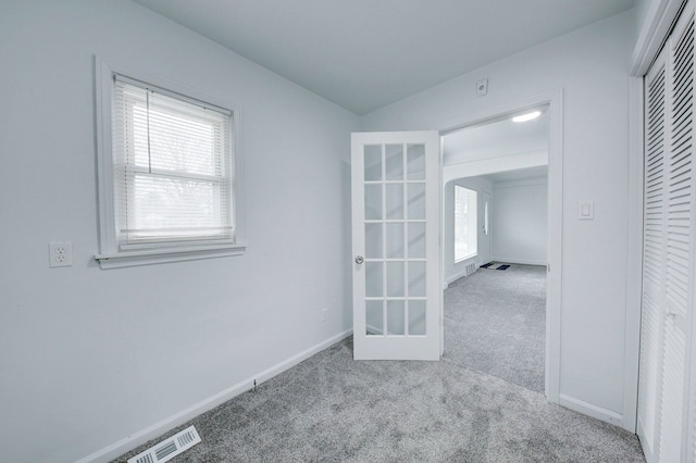 empty room featuring carpet floors, baseboards, arched walkways, and french doors