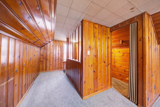 hallway featuring carpet floors, lofted ceiling, and wood walls