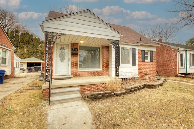 bungalow-style house with a shingled roof, a porch, and brick siding