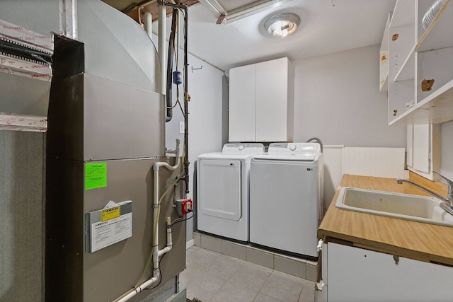 laundry room featuring cabinet space, light tile patterned floors, heating unit, separate washer and dryer, and a sink