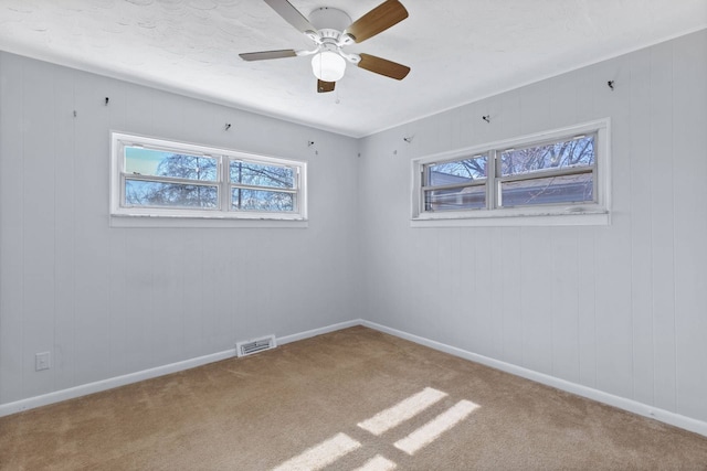 carpeted empty room with baseboards, visible vents, and a ceiling fan