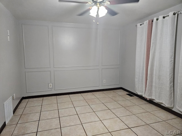 empty room featuring a ceiling fan, light tile patterned flooring, visible vents, and a decorative wall