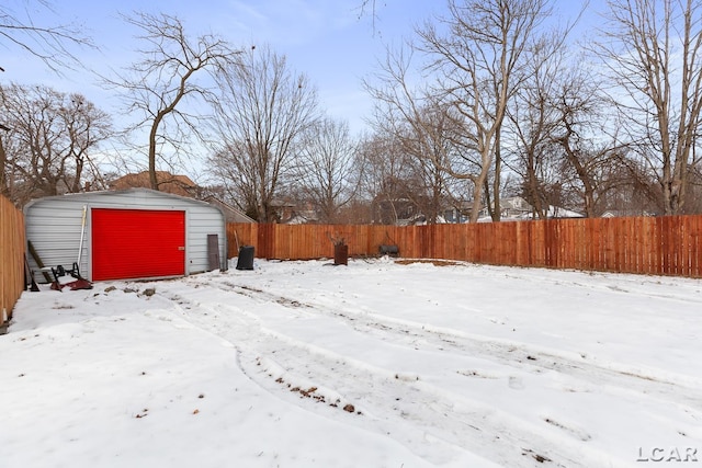 snowy yard featuring a garage, a fenced backyard, and an outdoor structure