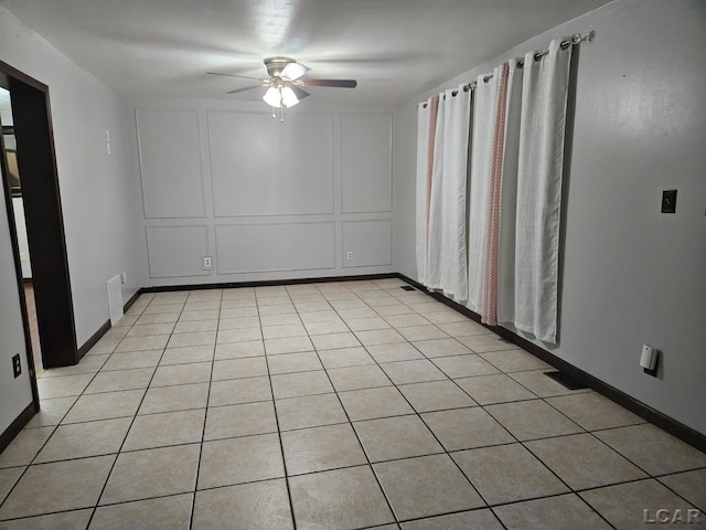 empty room featuring light tile patterned floors, visible vents, a decorative wall, ceiling fan, and baseboards