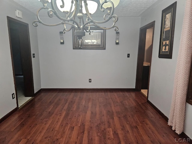 unfurnished dining area with dark wood-type flooring, a notable chandelier, a textured ceiling, and baseboards