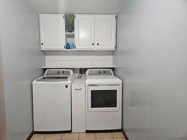 laundry area with a textured ceiling, separate washer and dryer, light tile patterned flooring, and cabinet space