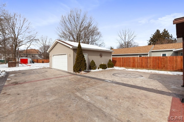 view of side of home featuring an outbuilding, concrete driveway, a detached garage, and fence